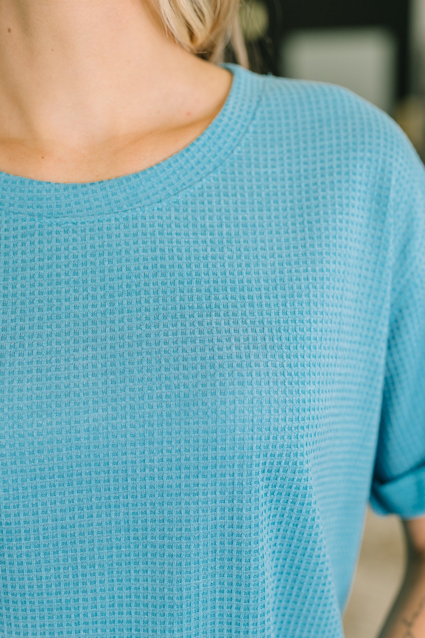 Close-up of a person wearing a textured blue sweater with a blurred background