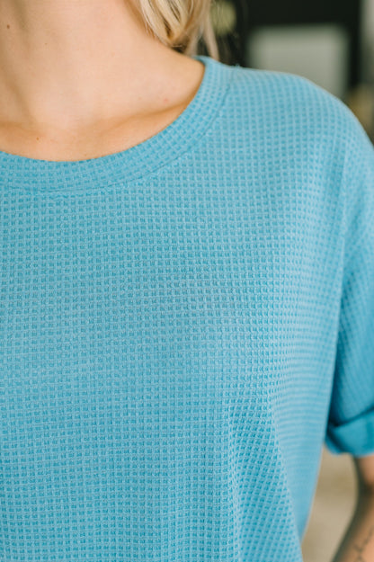 Close-up of a person wearing a textured blue sweater with a blurred background