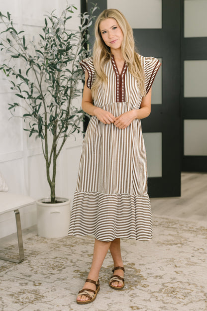 Woman wearing a striped dress standing indoors with a plant in the background