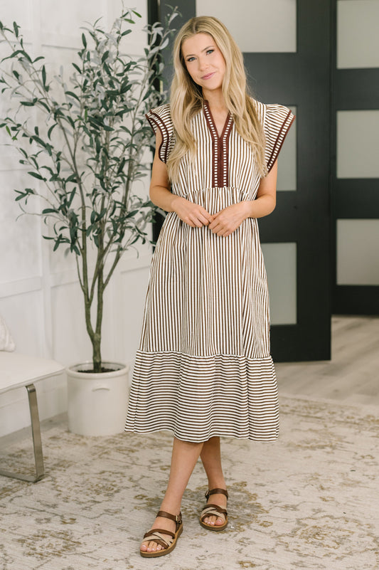 Woman wearing a striped dress standing indoors with a plant in the background