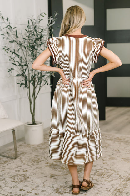 Woman wearing a striped dress in a room with a plant and bench.