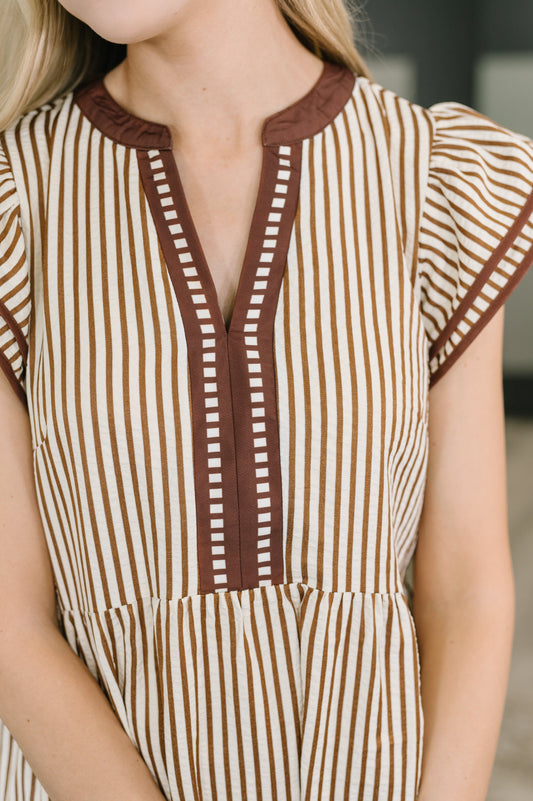 Close-up of a person wearing a brown and white striped dress with a V-neckline.