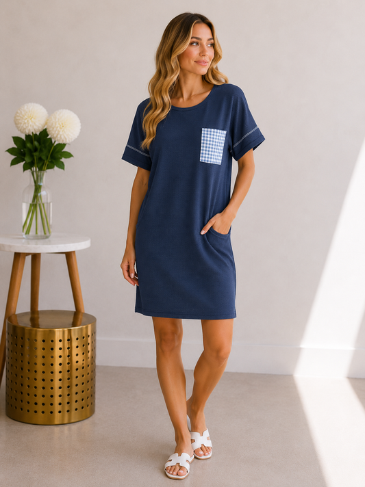 Woman wearing a navy blue dress with a pocket, standing in a room with a white wall and a small table with flowers.