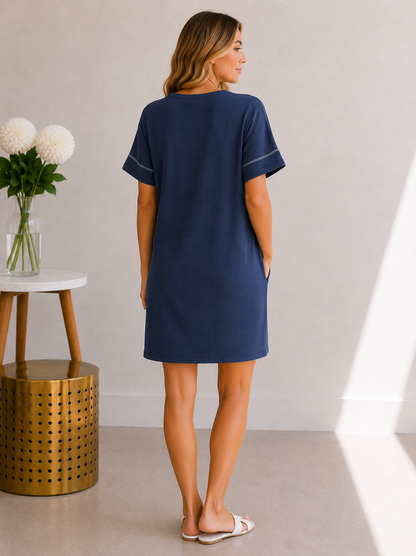 Woman wearing a navy blue dress standing in a minimalistic room with a vase of flowers on a table.