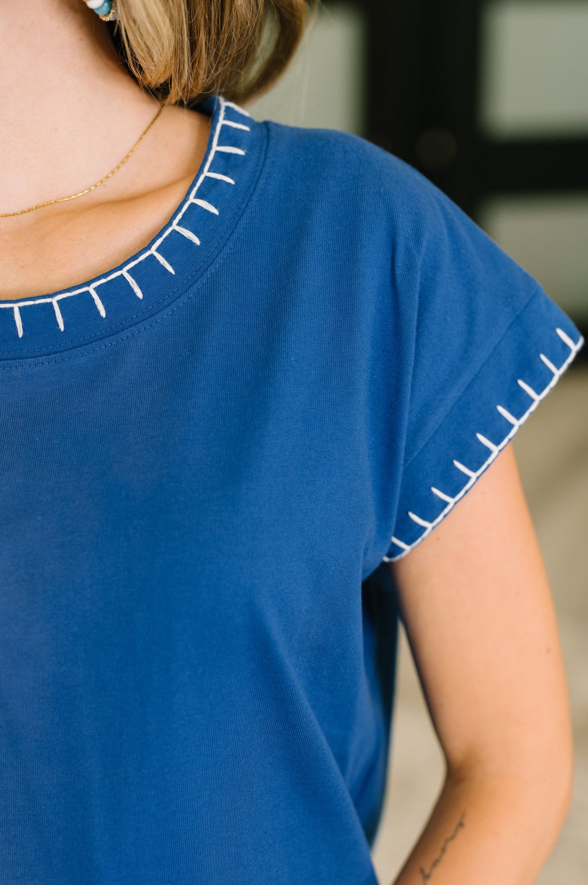 Close-up of a person wearing a royal blue short-sleeve top with white contrast stitching along the neckline and sleeve cuffs.