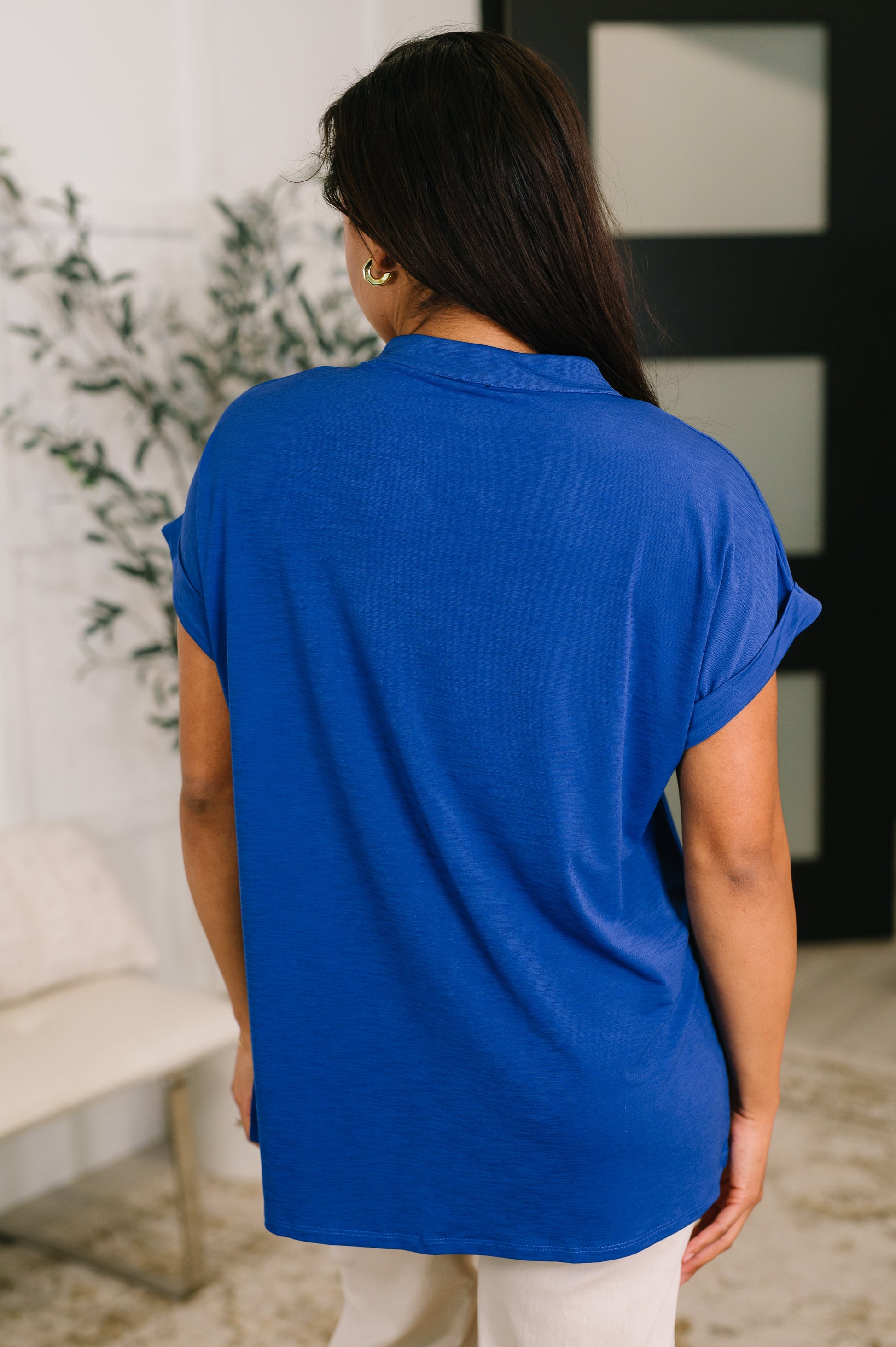 Person wearing a blue top in an indoor setting with plants and furniture.