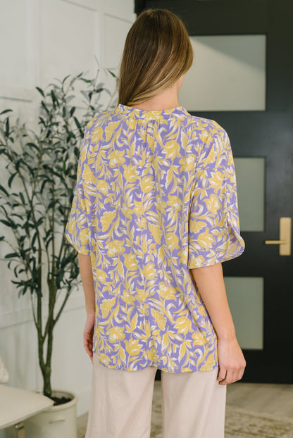Woman wearing a yellow and purple patterned blouse in an indoor setting.