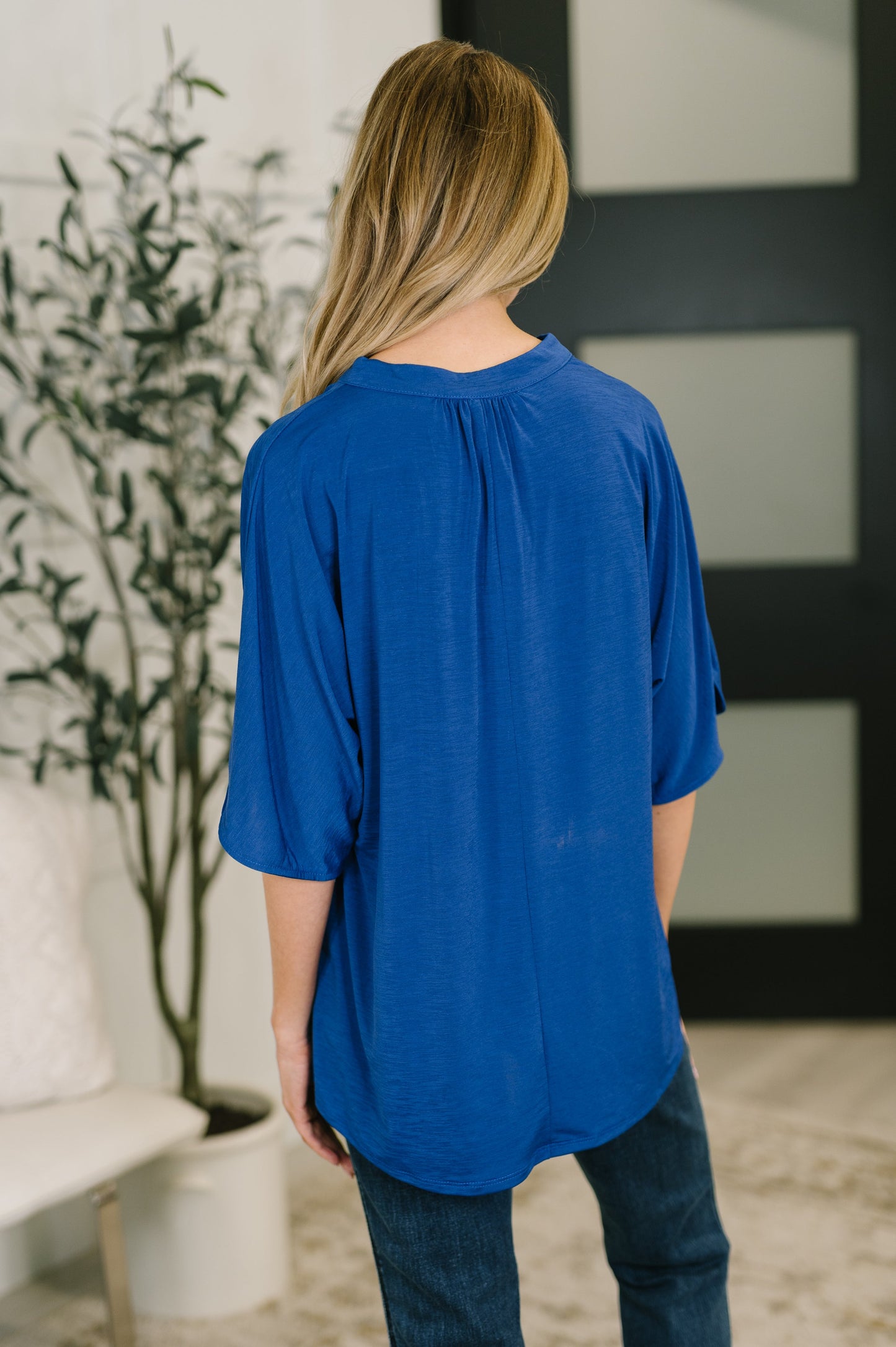Person wearing a blue top in an indoor setting with a plant and white wall in the background