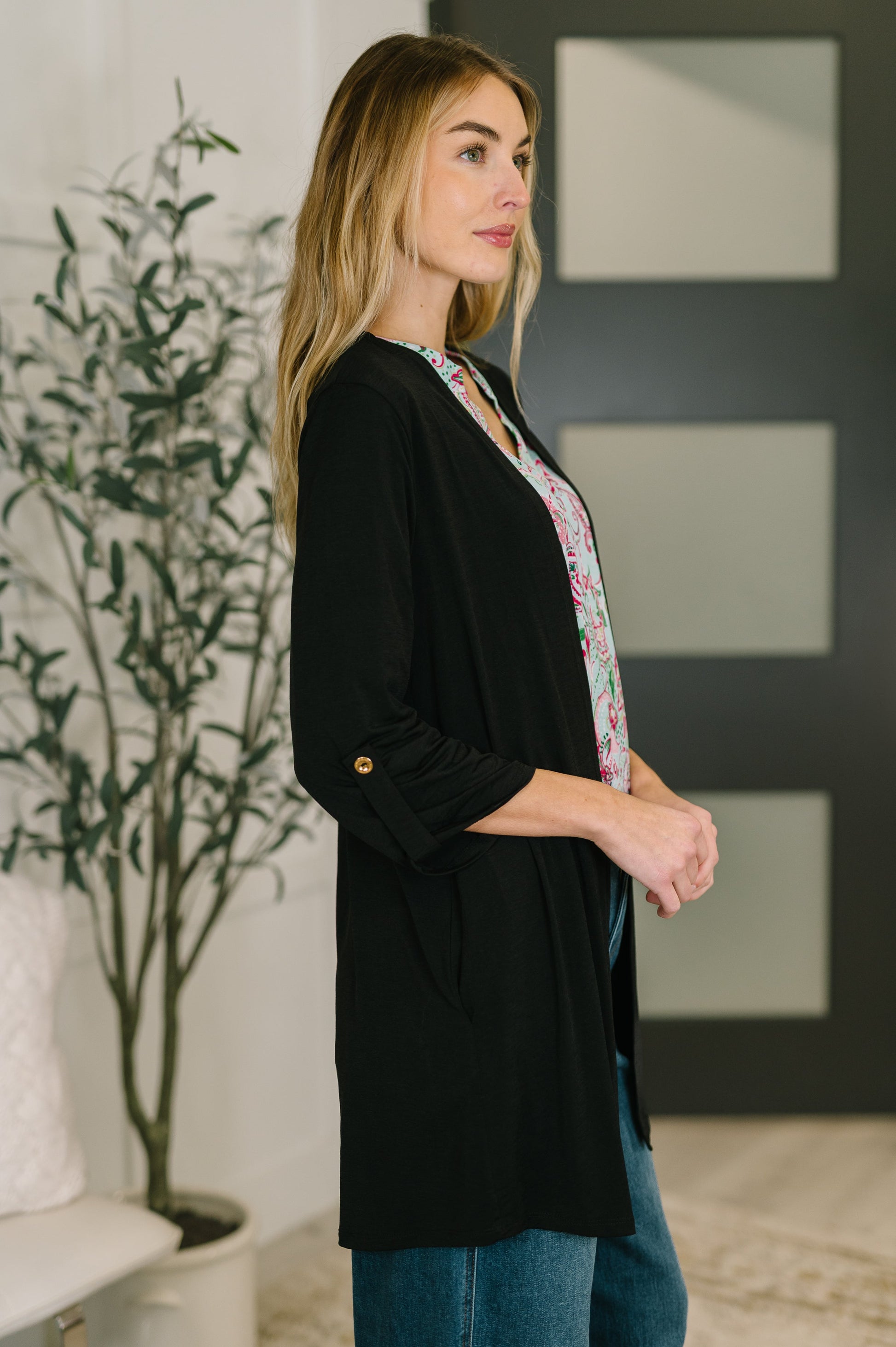 Woman wearing a black cardigan over a floral top in an indoor setting.