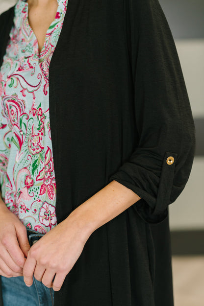 Person wearing a black cardigan over a colorful patterned shirt with a blurred background