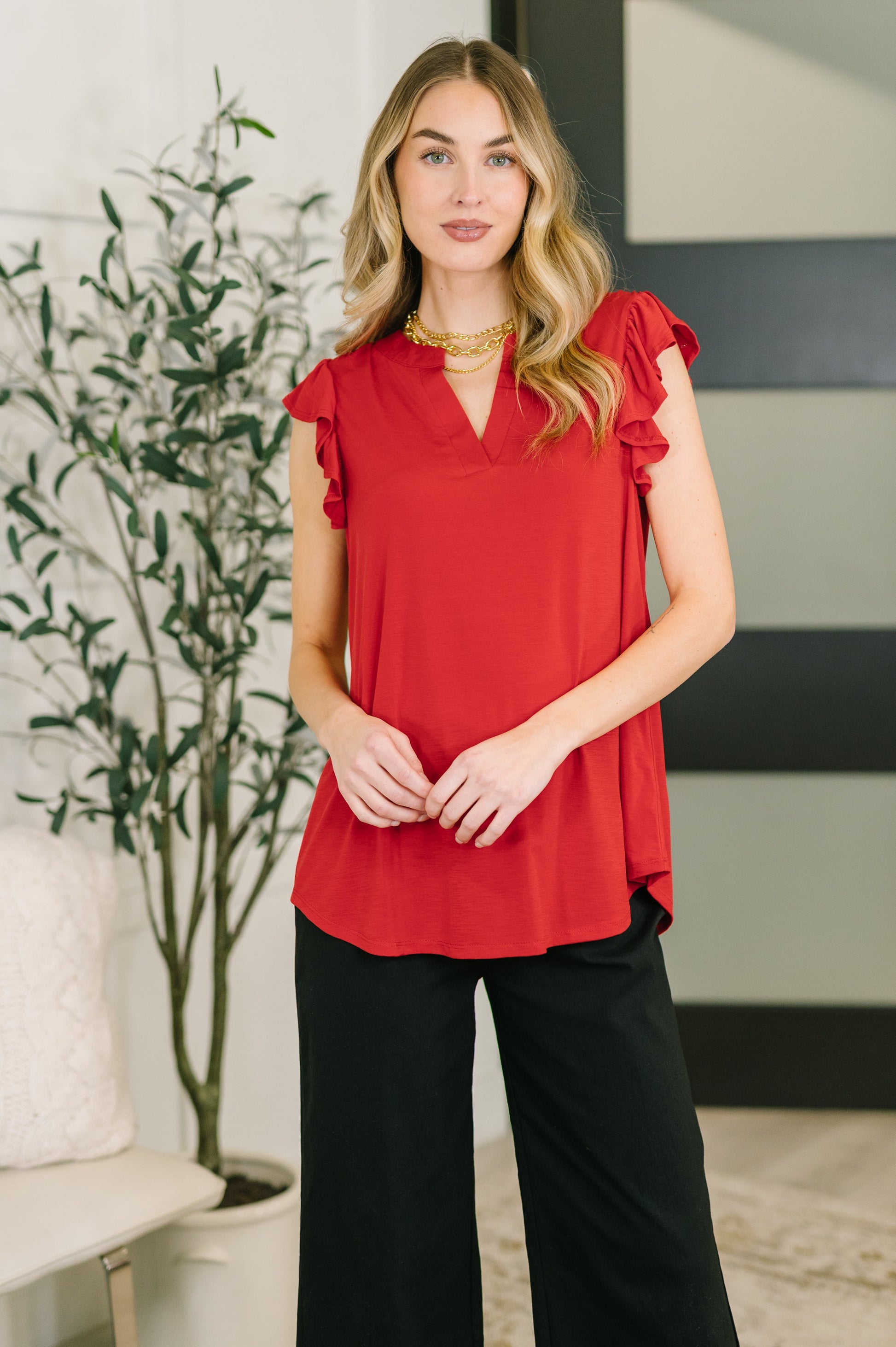 Woman wearing a red blouse with ruffled sleeves and black pants in an indoor setting.