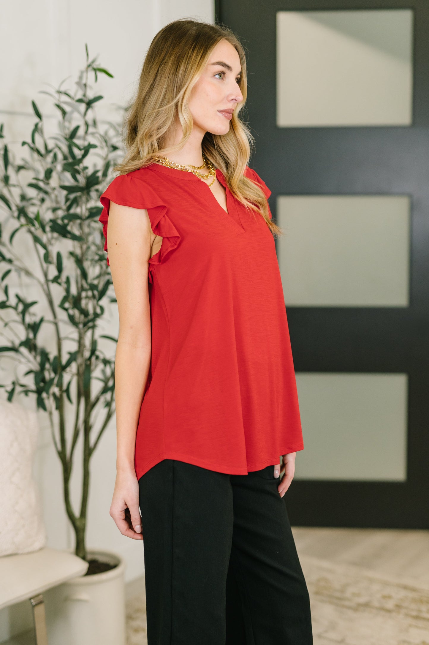 Woman wearing a red blouse with ruffled sleeves in an indoor setting.