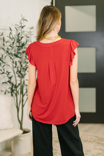 Woman wearing a red top and black pants in an indoor setting with a plant and wall art.