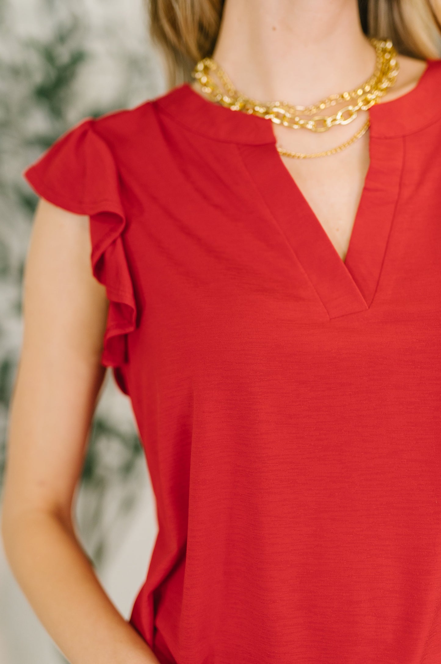 Red top with ruffled sleeves and gold necklace on a blurred background