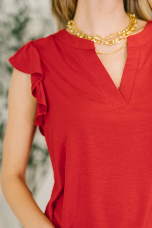 Red top with ruffled sleeves and gold necklace on a blurred background