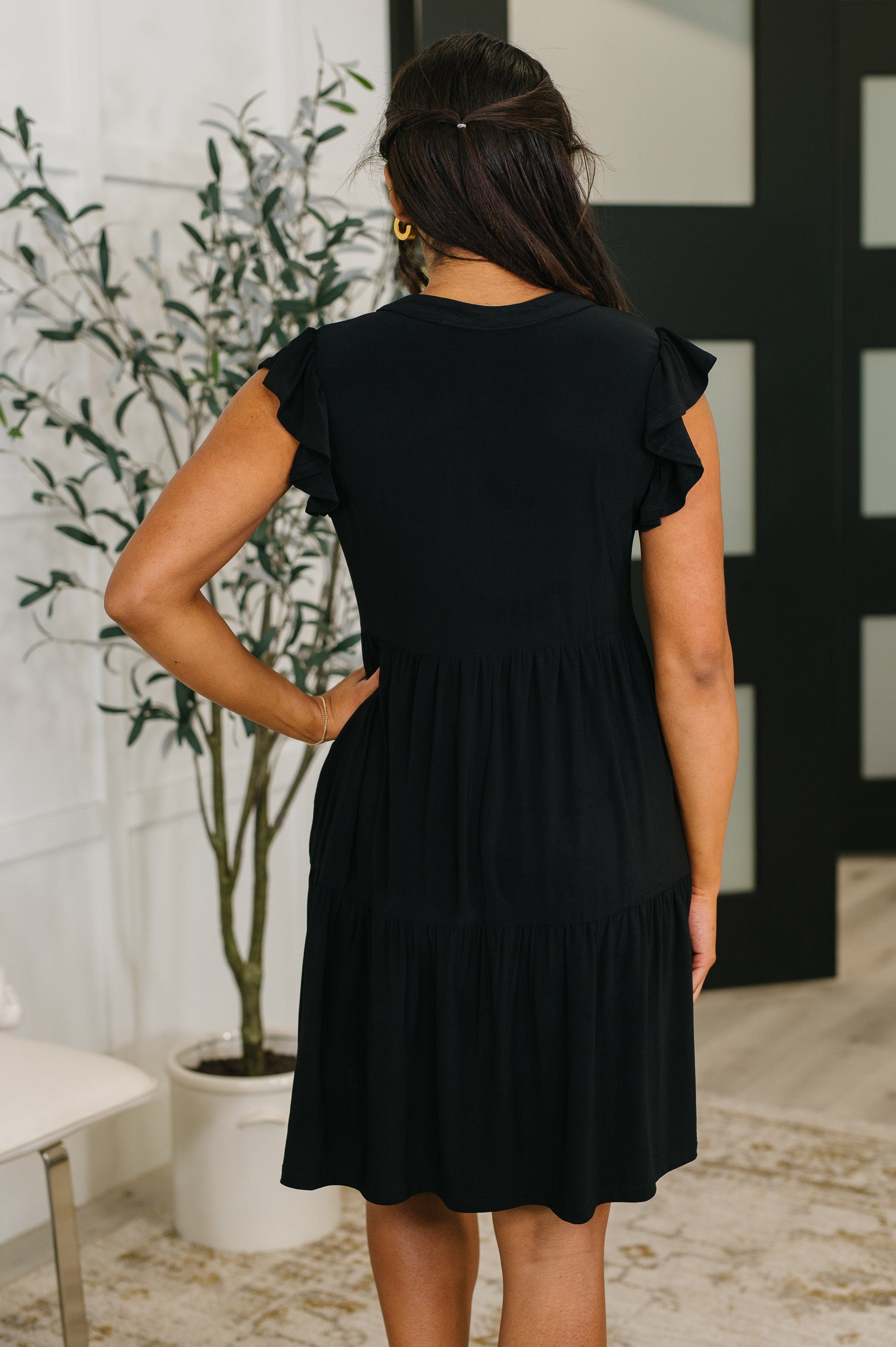 Woman wearing a black dress with ruffled sleeves in an indoor setting.