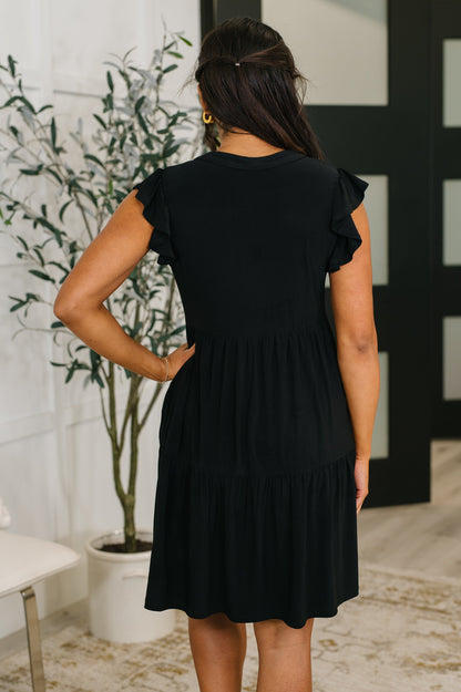 Woman wearing a black dress with ruffled sleeves in an indoor setting.