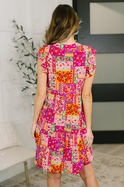 Woman wearing a colorful patchwork dress in a room with a plant and sofa.