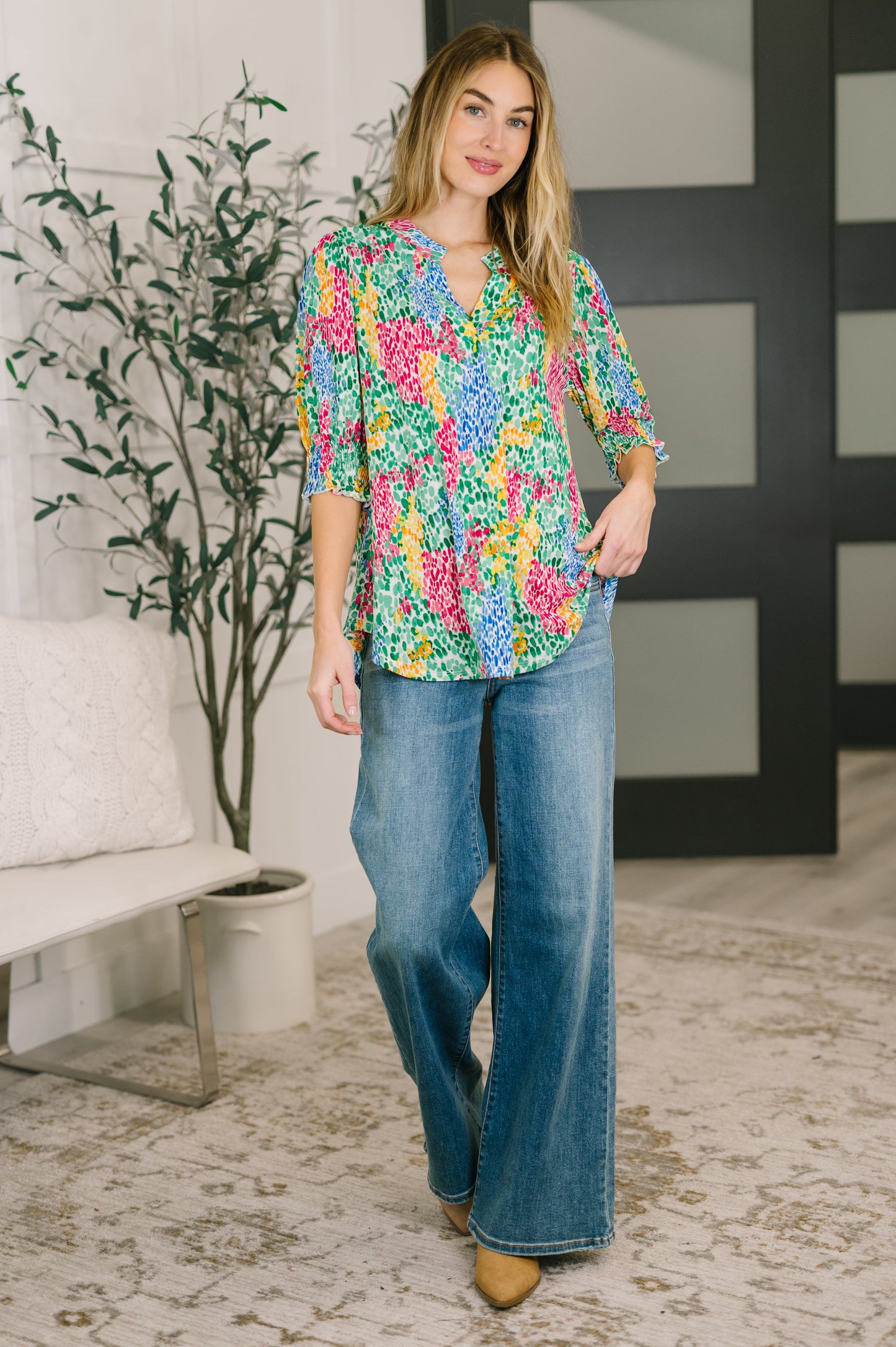 Woman wearing a colorful floral blouse and blue jeans in a living room setting.