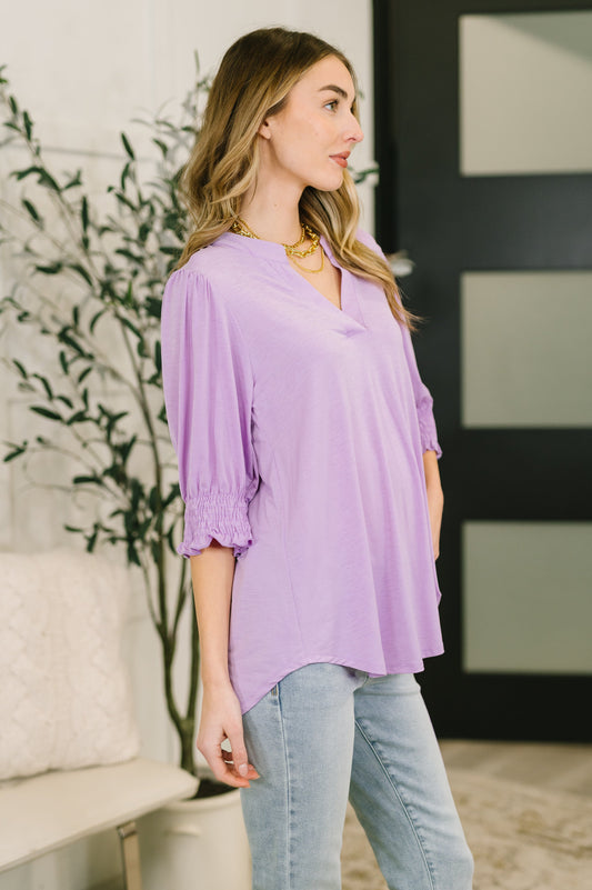Woman wearing a purple blouse and light blue jeans indoors.