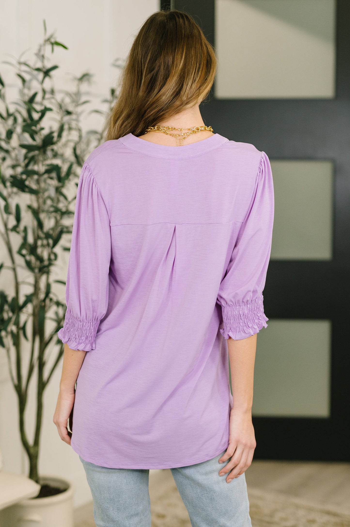 Woman wearing a purple blouse with rolled-up sleeves in an indoor setting.