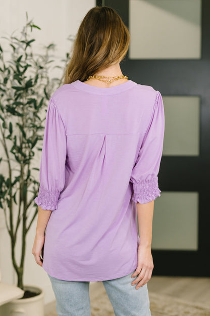Woman wearing a purple blouse with rolled-up sleeves in an indoor setting.