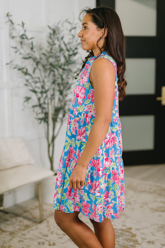Woman wearing a colorful floral dress in a room with a plant and door.