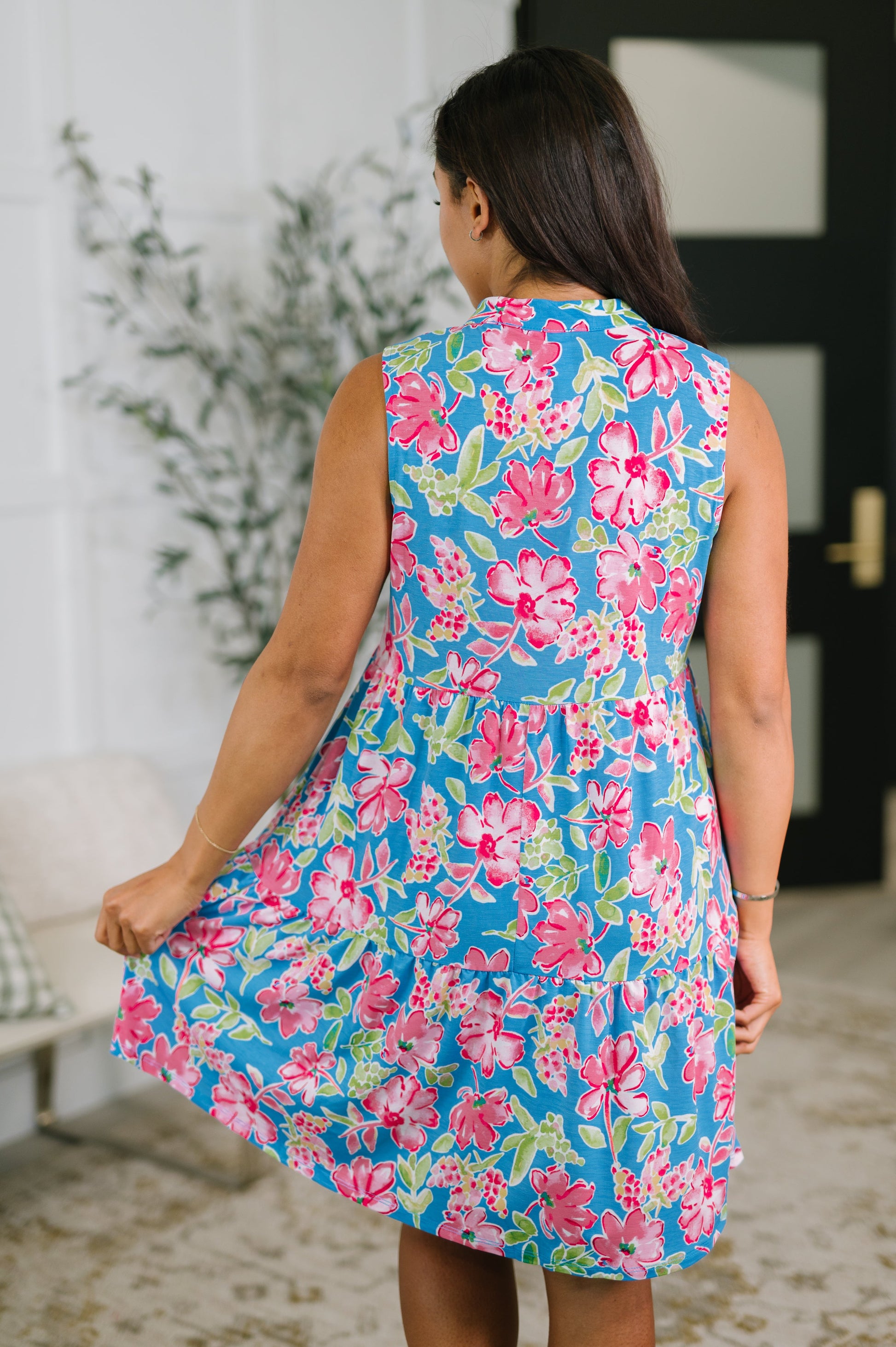 Woman wearing a floral dress in a room with a plant and door in the background