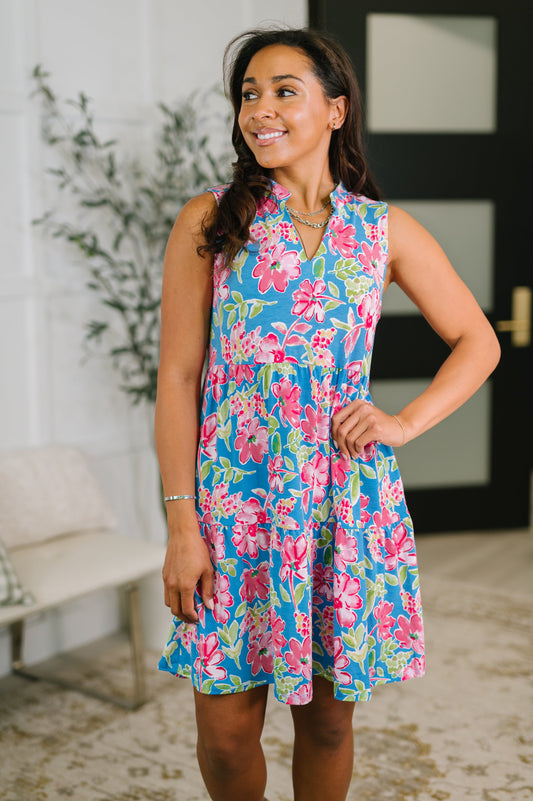 Woman wearing a floral dress standing indoors with a plant and door in the background