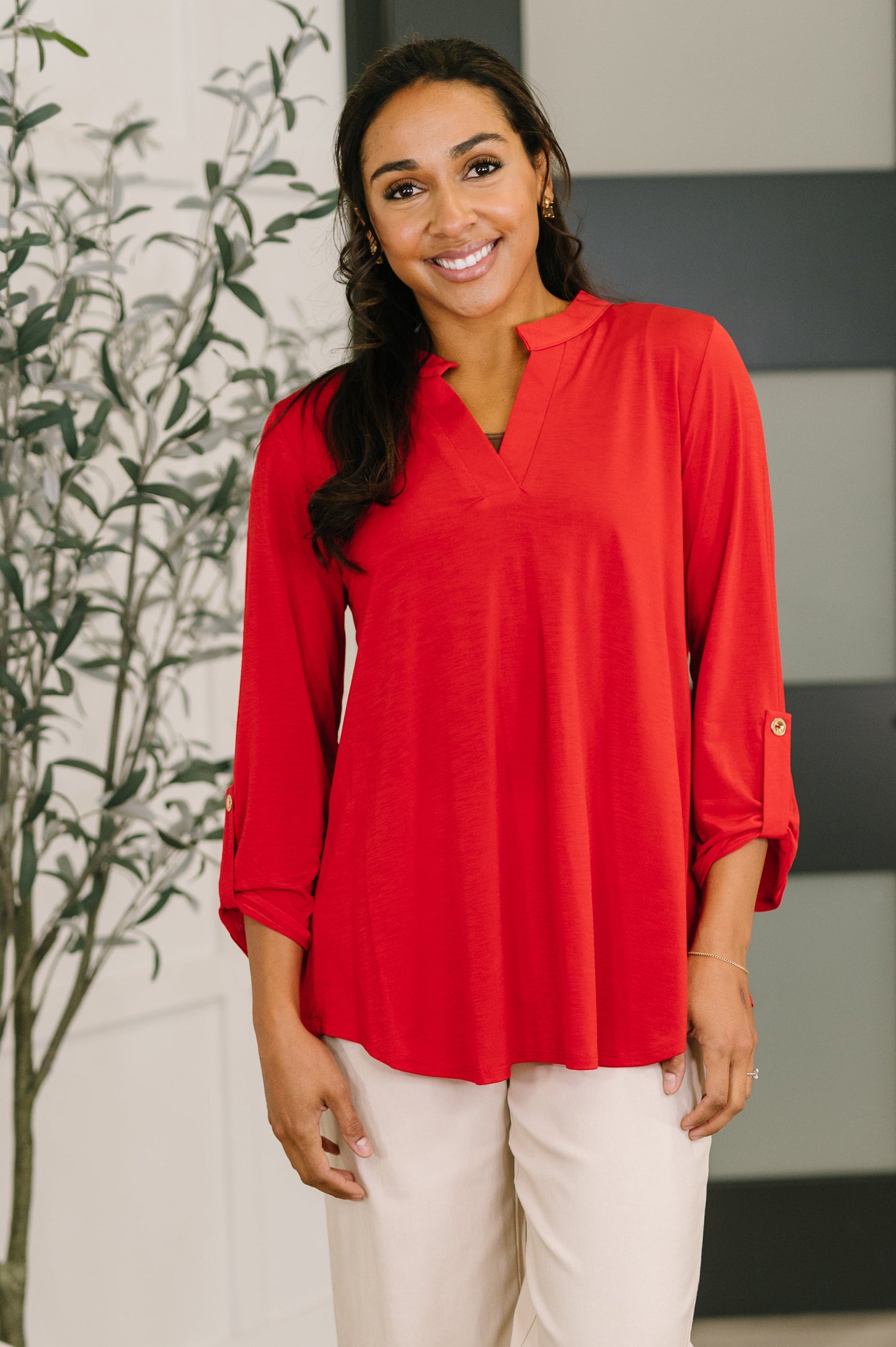Woman wearing a red blouse standing indoors with a plant in the background
