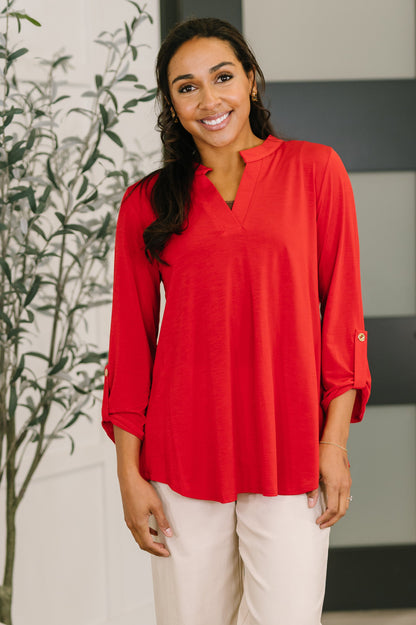 Woman wearing a red blouse standing indoors with a plant in the background