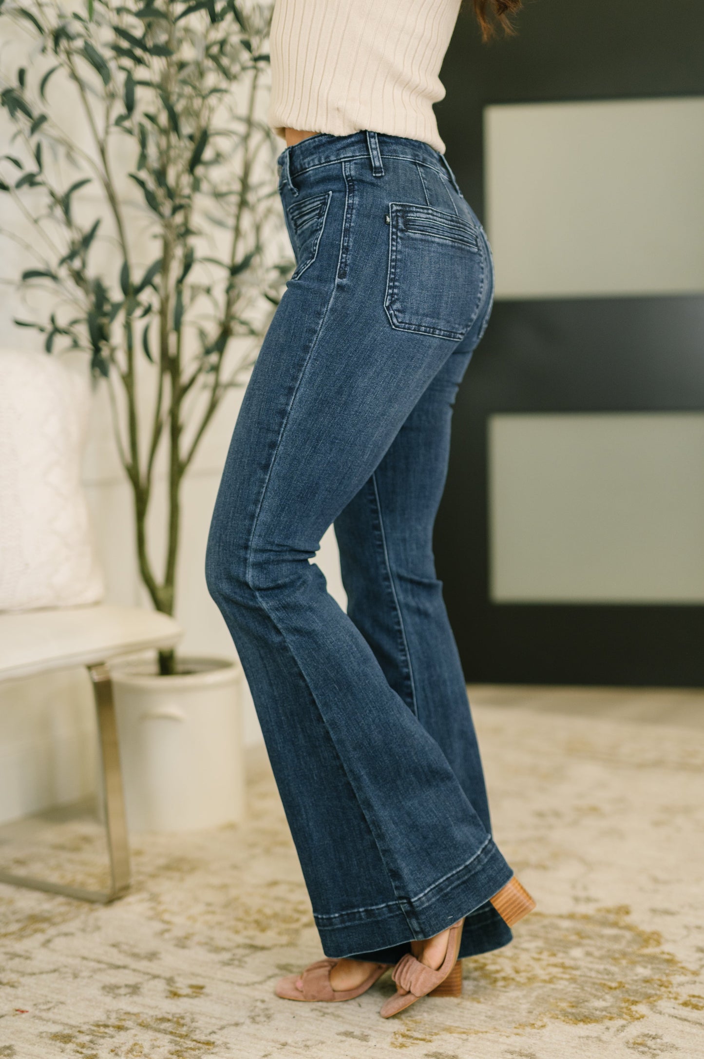 Person wearing blue jeans in a room with a plant and a chair.