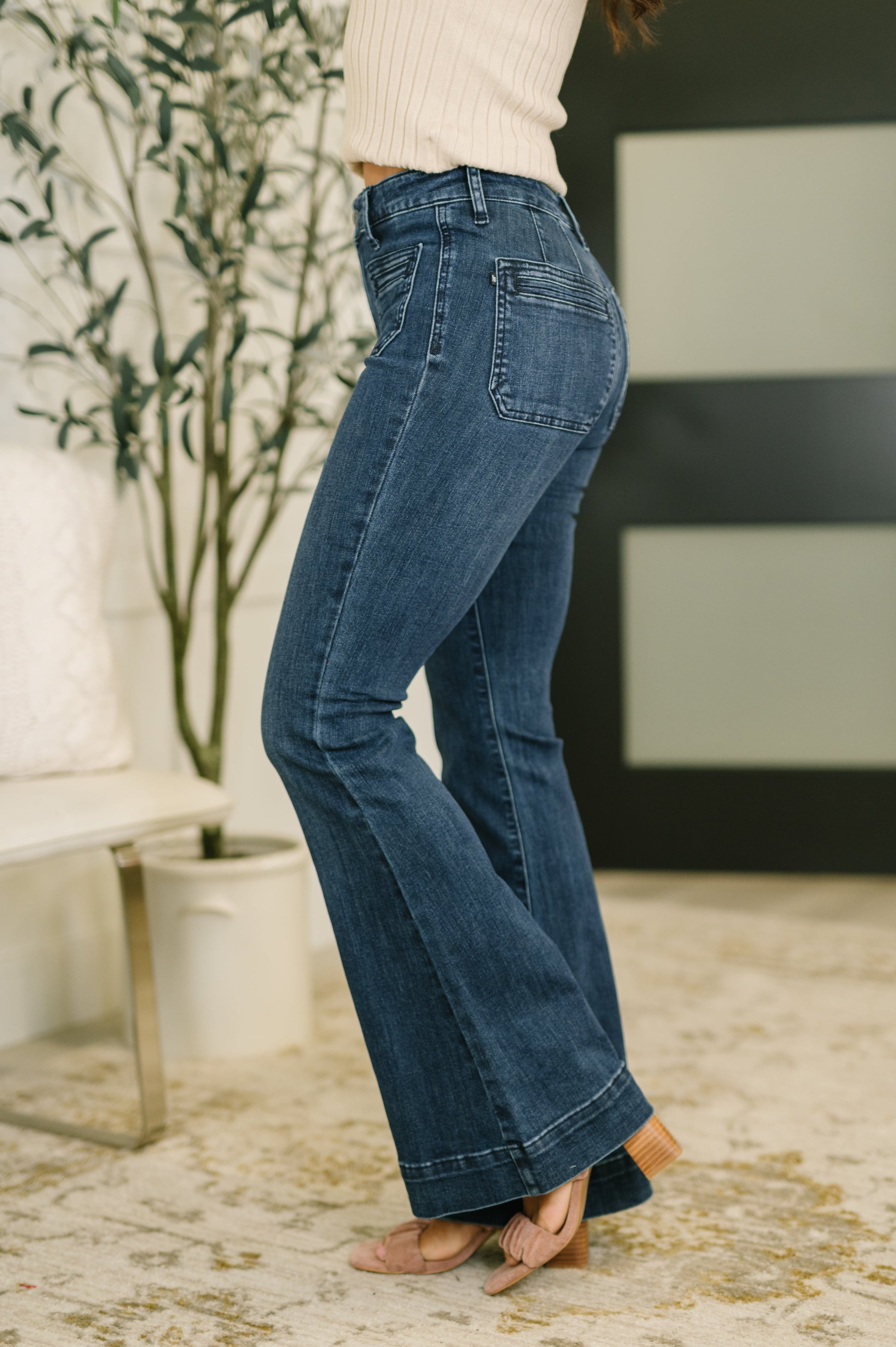 Person wearing blue jeans in a room with a plant and a chair.