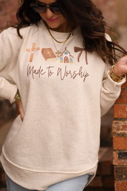 Person wearing a beige sweatshirt with 'Made to Worship' text and religious symbols.