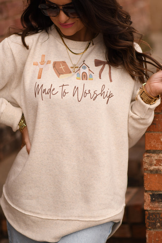 Person wearing a beige sweatshirt with 'Made to Worship' text and religious symbols.