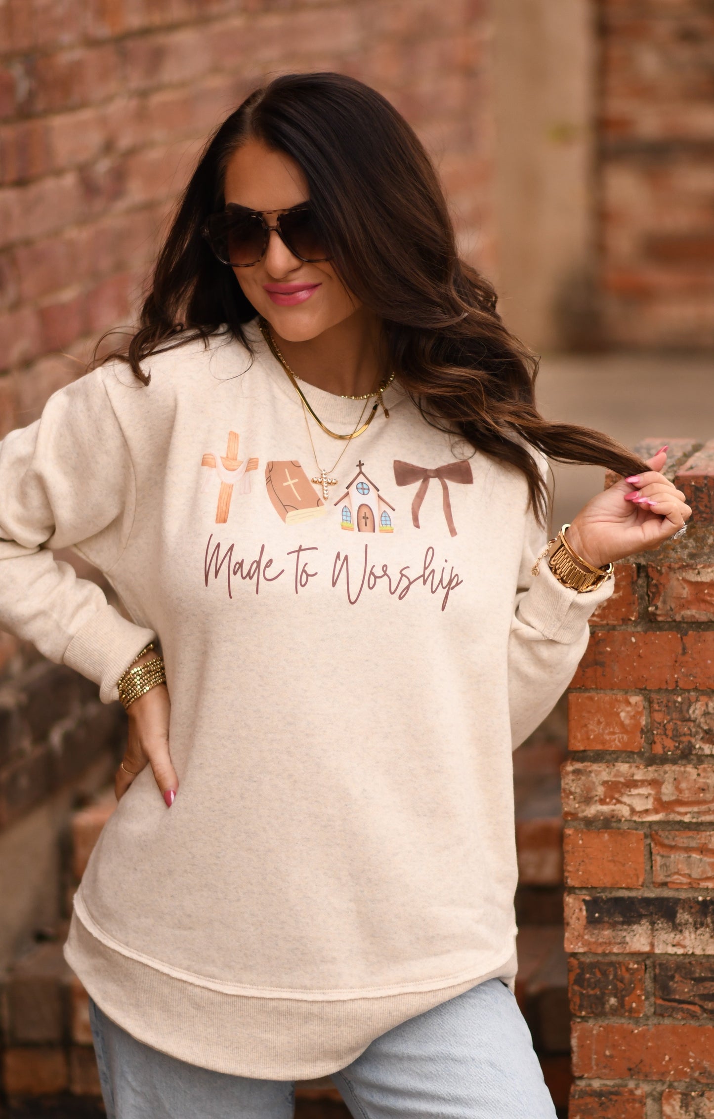 Woman wearing a beige sweatshirt with text and graphics against a brick wall.