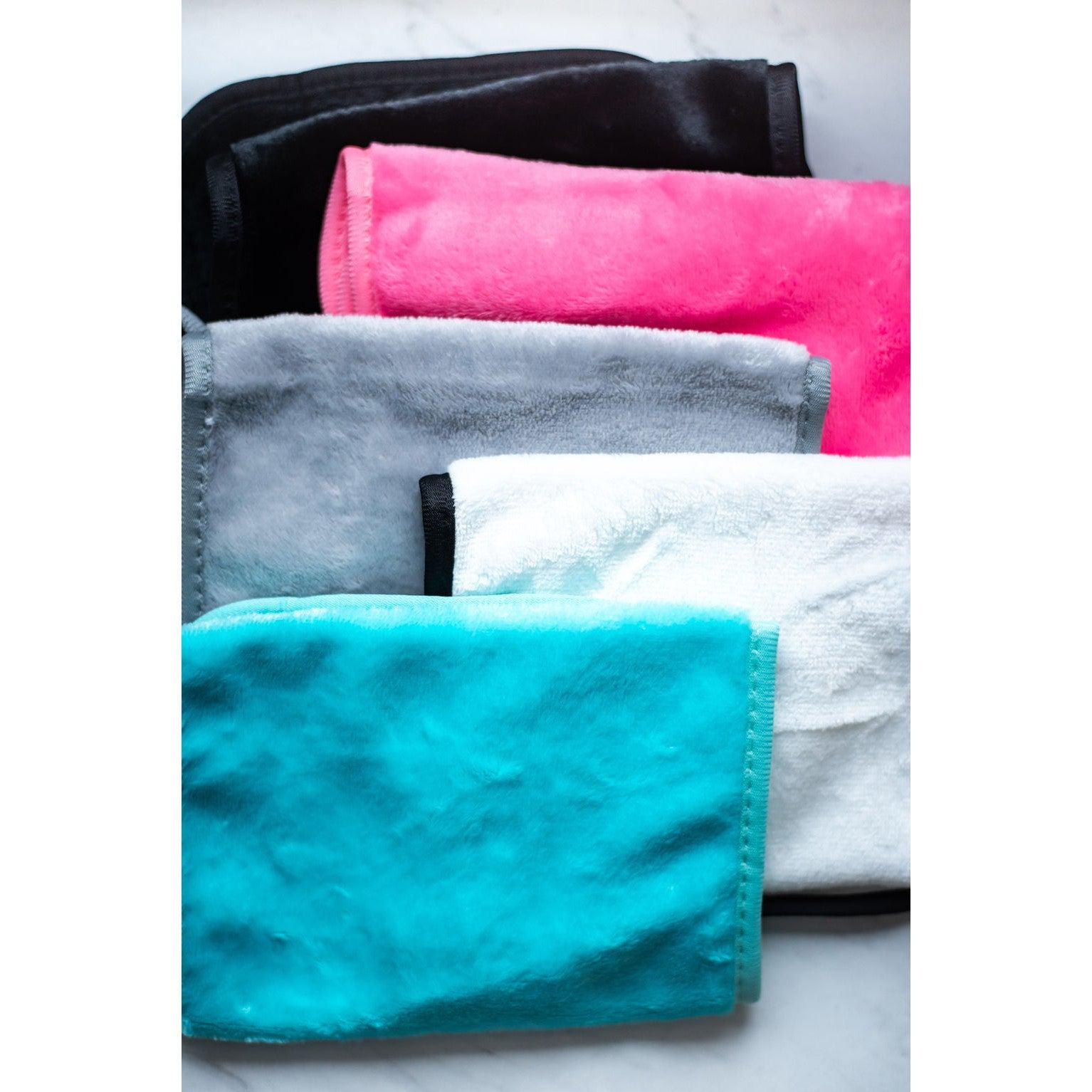 Stack of folded towels in black, pink, gray, white, and blue on a white background