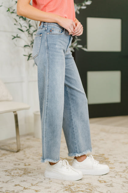 Person wearing light blue jeans and white sneakers in a room with a plant and a blackboard.