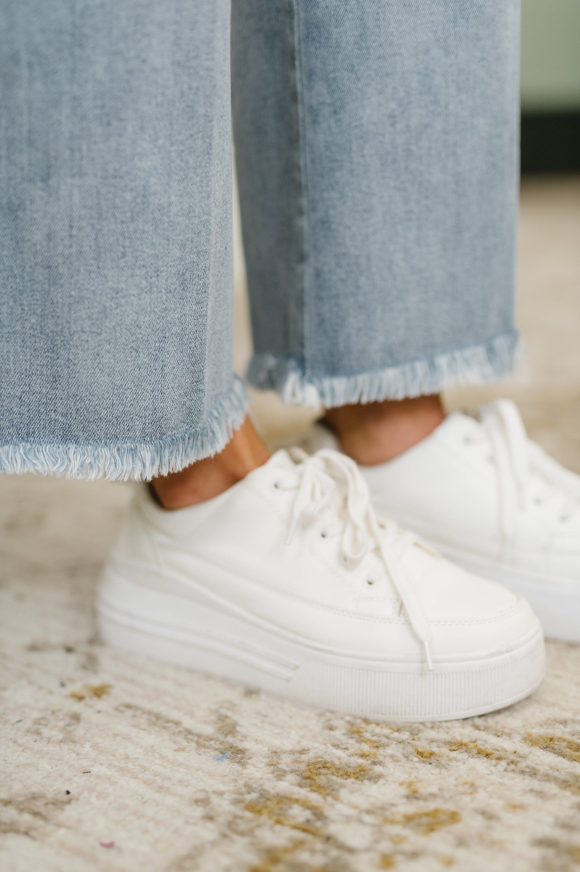 White sneakers worn with light blue jeans on a patterned carpet
