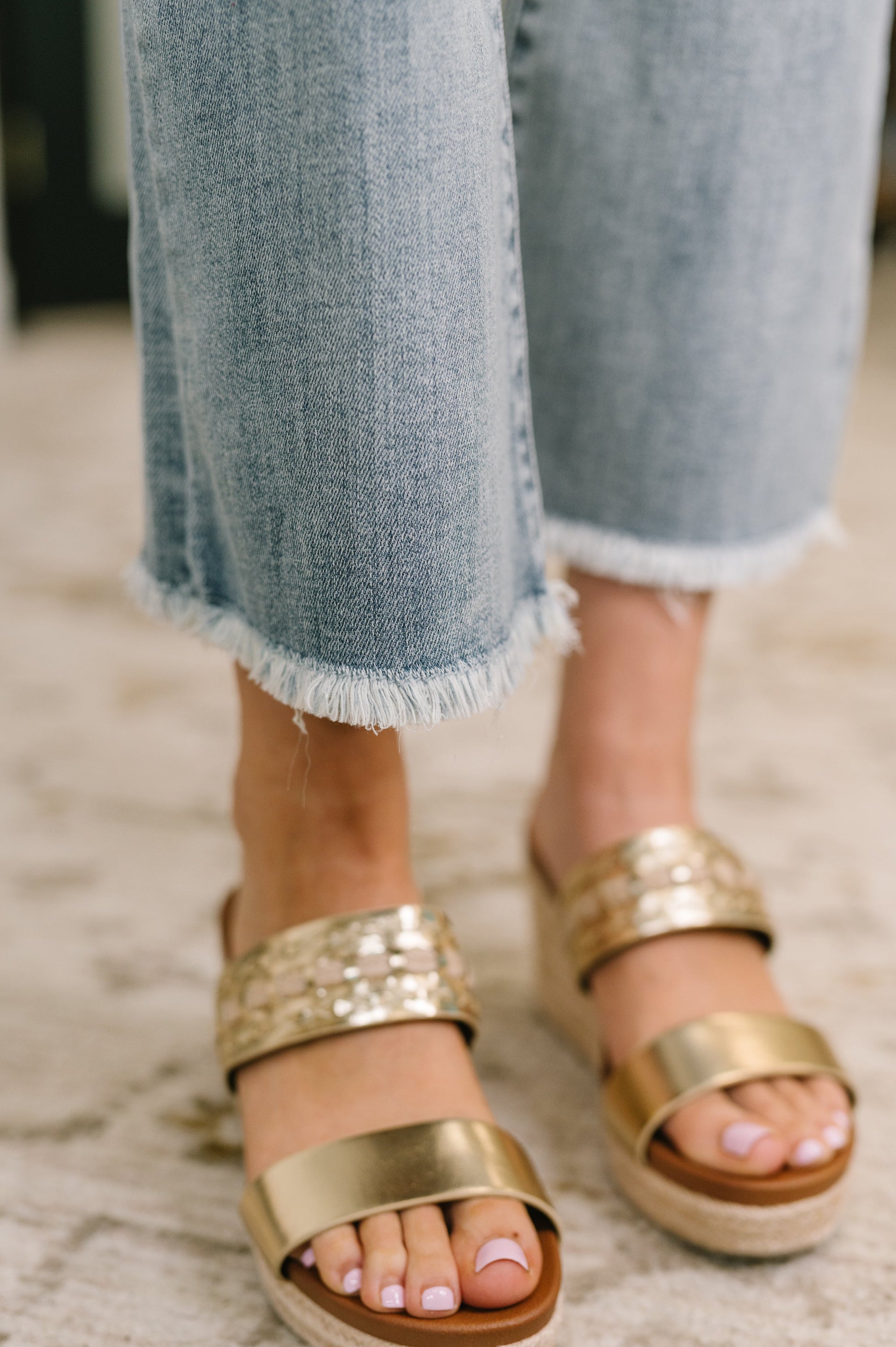 Gold sandals worn with light blue jeans on a neutral background