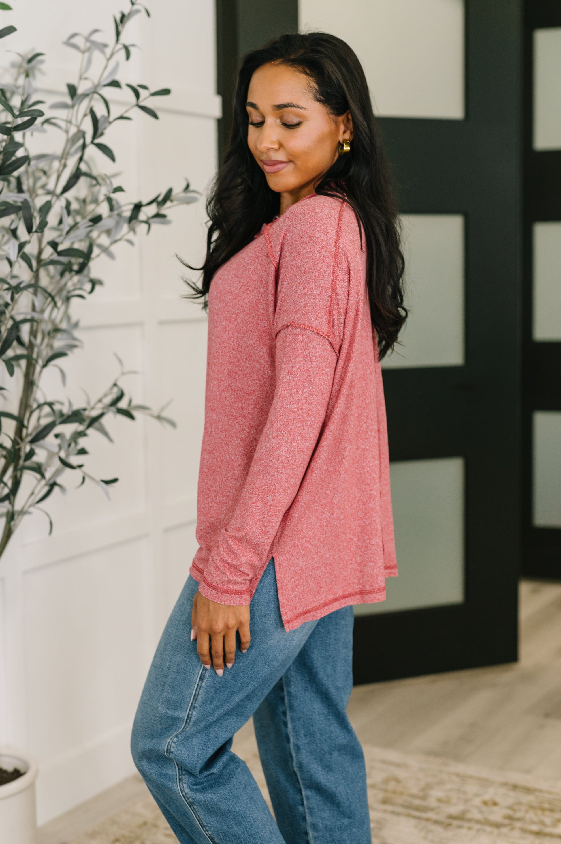 Woman wearing a pink long-sleeve top and blue jeans standing indoors.