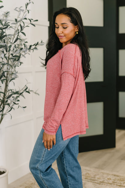 Woman wearing a pink long-sleeve top and blue jeans standing indoors.