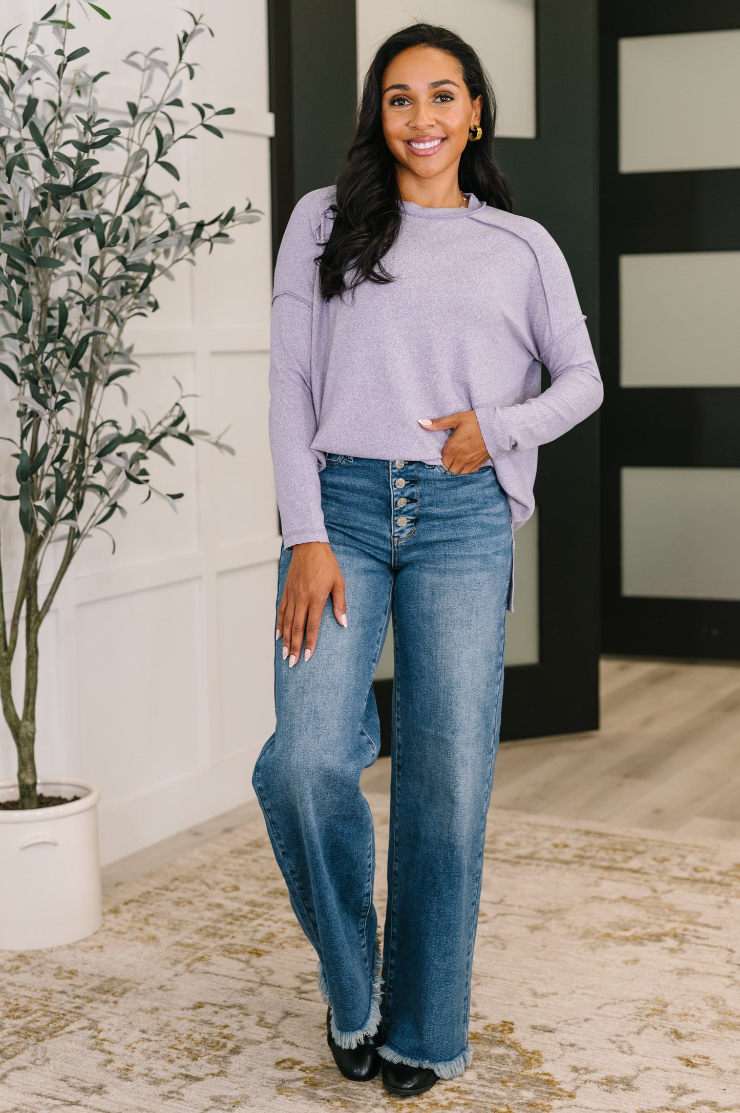 Woman wearing a light purple sweater and blue jeans standing indoors.