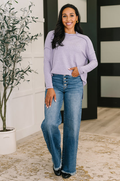 Woman wearing a light purple sweater and blue jeans standing indoors.