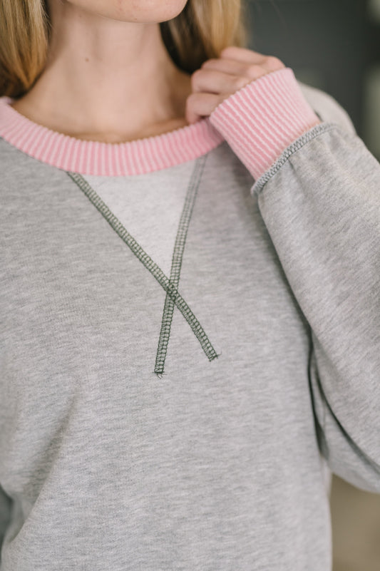 Gray sweatshirt with pink collar worn by a person, blurred background