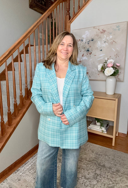 Woman in a light blue plaid blazer standing in a home interior with a staircase and decorative items.