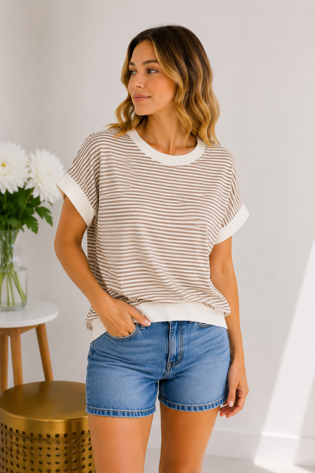 Woman wearing a striped shirt and denim shorts standing indoors with a neutral background