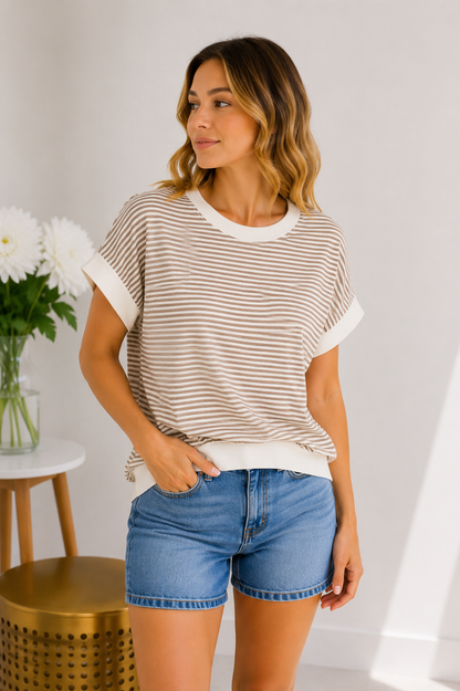 Woman wearing a striped shirt and denim shorts standing indoors with a neutral background
