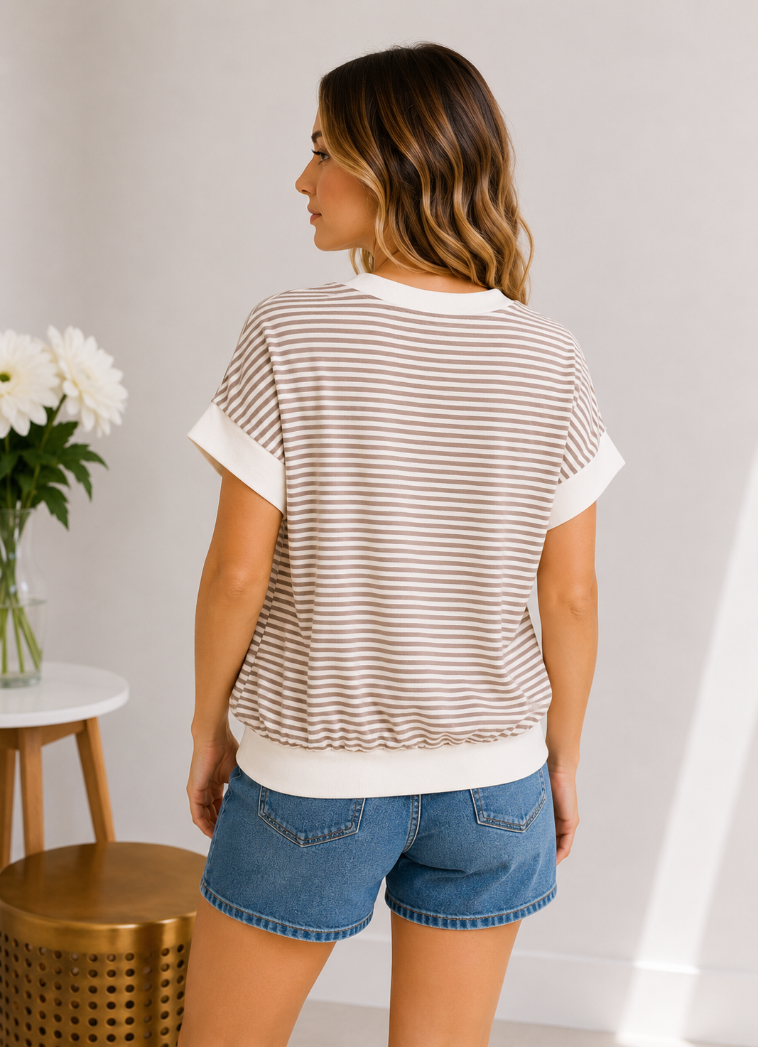 Woman wearing a striped shirt and denim shorts in a minimal indoor setting.
