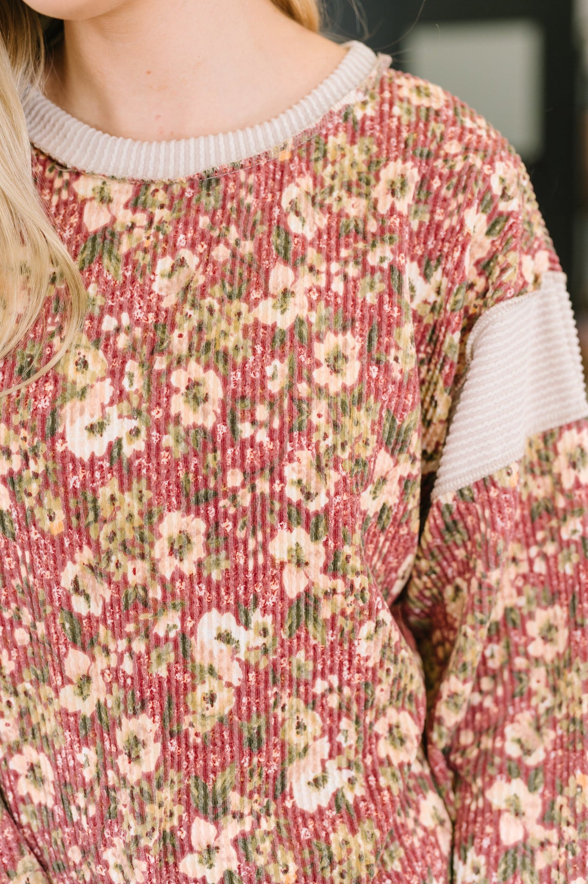Close-up of a person wearing a ribbed knit sweater with a muted pink and green floral pattern and contrasting light beige ribbed trim.